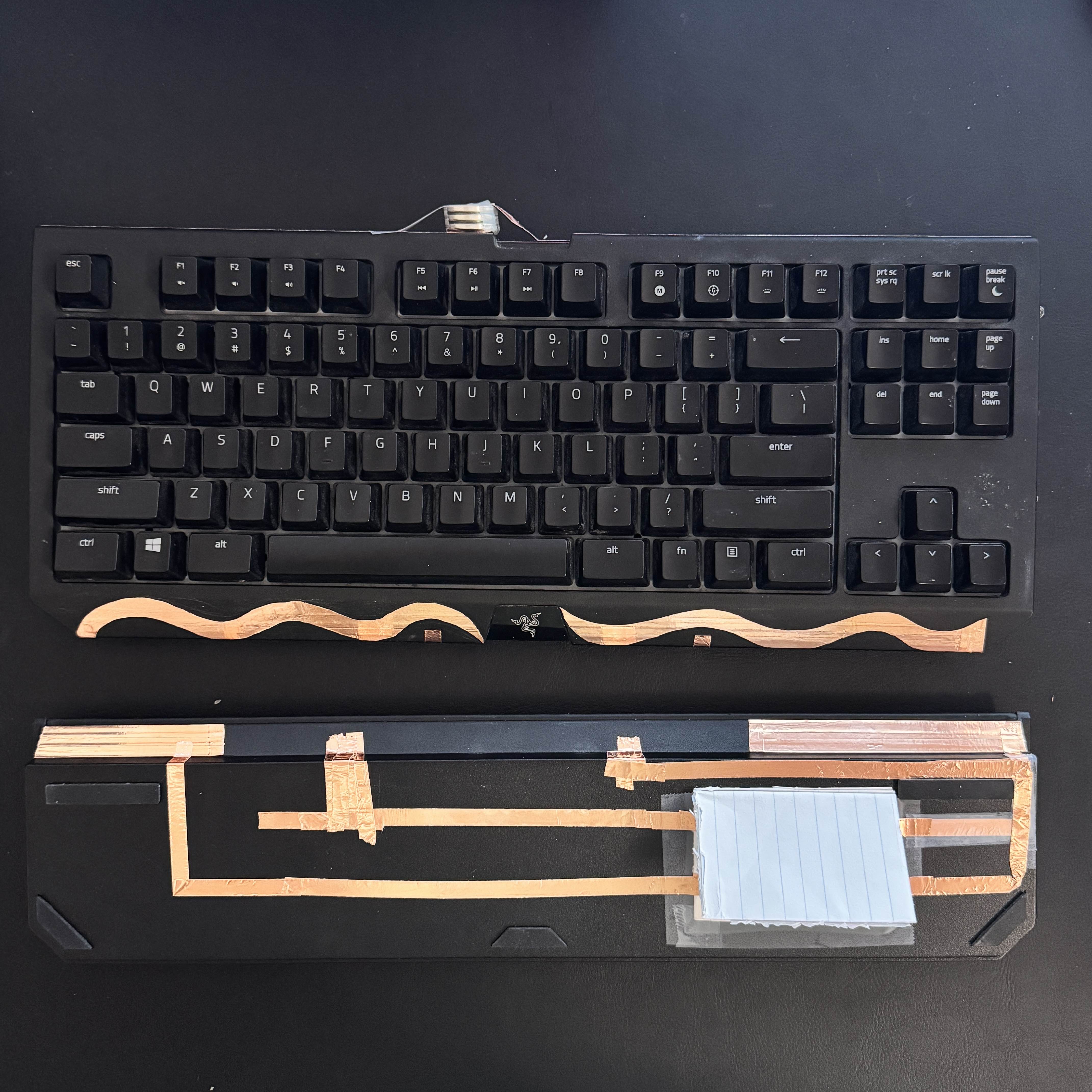 <a href='https://youtube.com/shorts/capjBhhHXBQ?si=WQM_WKlzxtzjt1T6' target='_blank'><p>Demo Video Link</p></a> This circuit senses the weight of your wrists on the rest through a paper switch. The keyboard has three batteries stacked on the back of its casing. There are three LEDs on each side of the keyboard (six total) that are powered with paralell copper tapes. These tapes are broken up and are only completed when the paper switch is pressed. The switch is featured on the left side of the keyboard for single-handed use when gaming. The copper wiring on the front is both stylish and functional since it's cut specifically to match the brand's swirly logo.