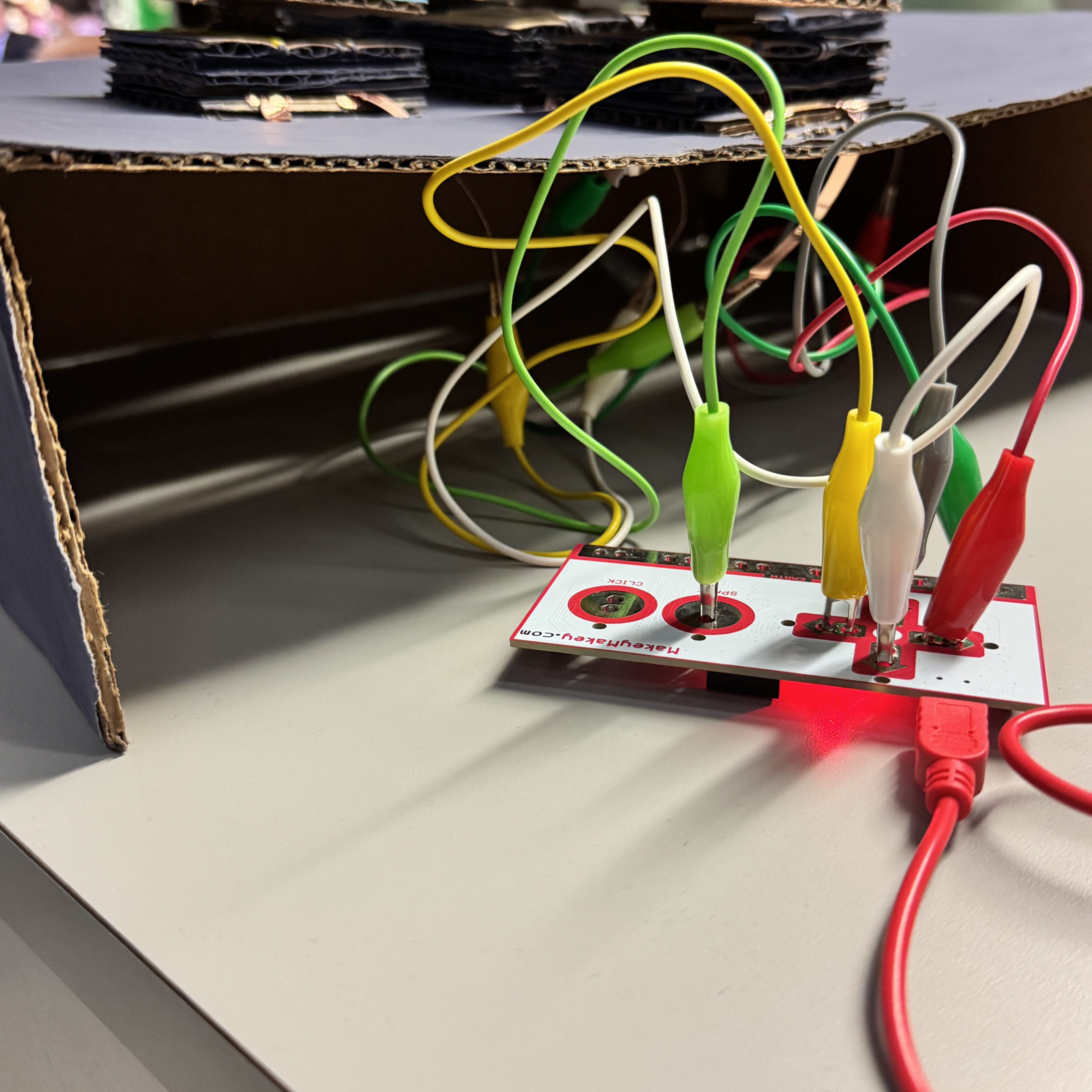 This is the back of the Makey-Makey setup. During Activity 2, I hated how messy everything looked with the wires, so I propped up the control panel and made it more like a box. I cut holes behind the buttons to connect copper tape extensions to the incomplete circuits. Each button was then connected to the proper key of the Makey-Makey, and one long copper tape piece connected each button to the ground wire.